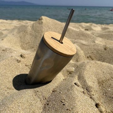 Термо чаша със сламка, заровена в пясъка на плажа
